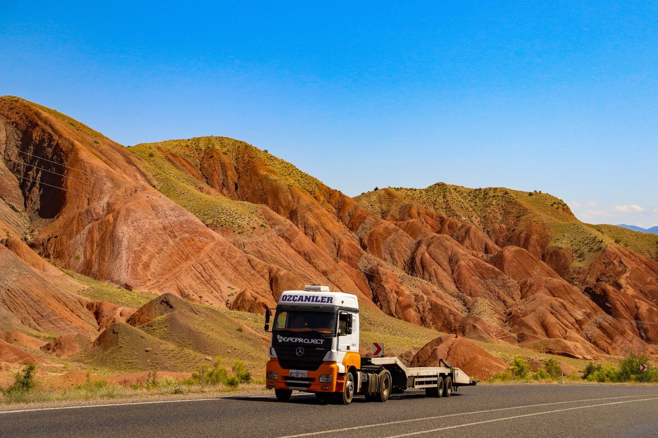 Truck passes through colorful mountain landscape under clear blue sky.